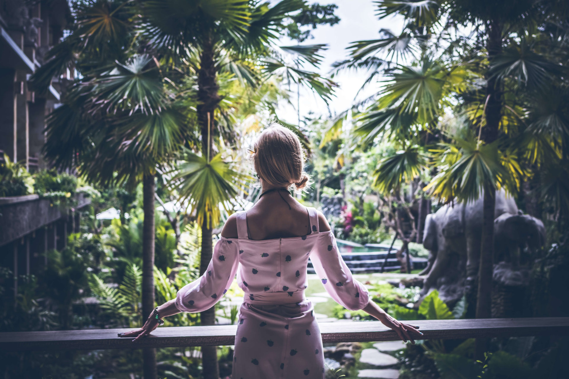 Woman in pink dress looking out at lush tropical garden in Bali travel destination